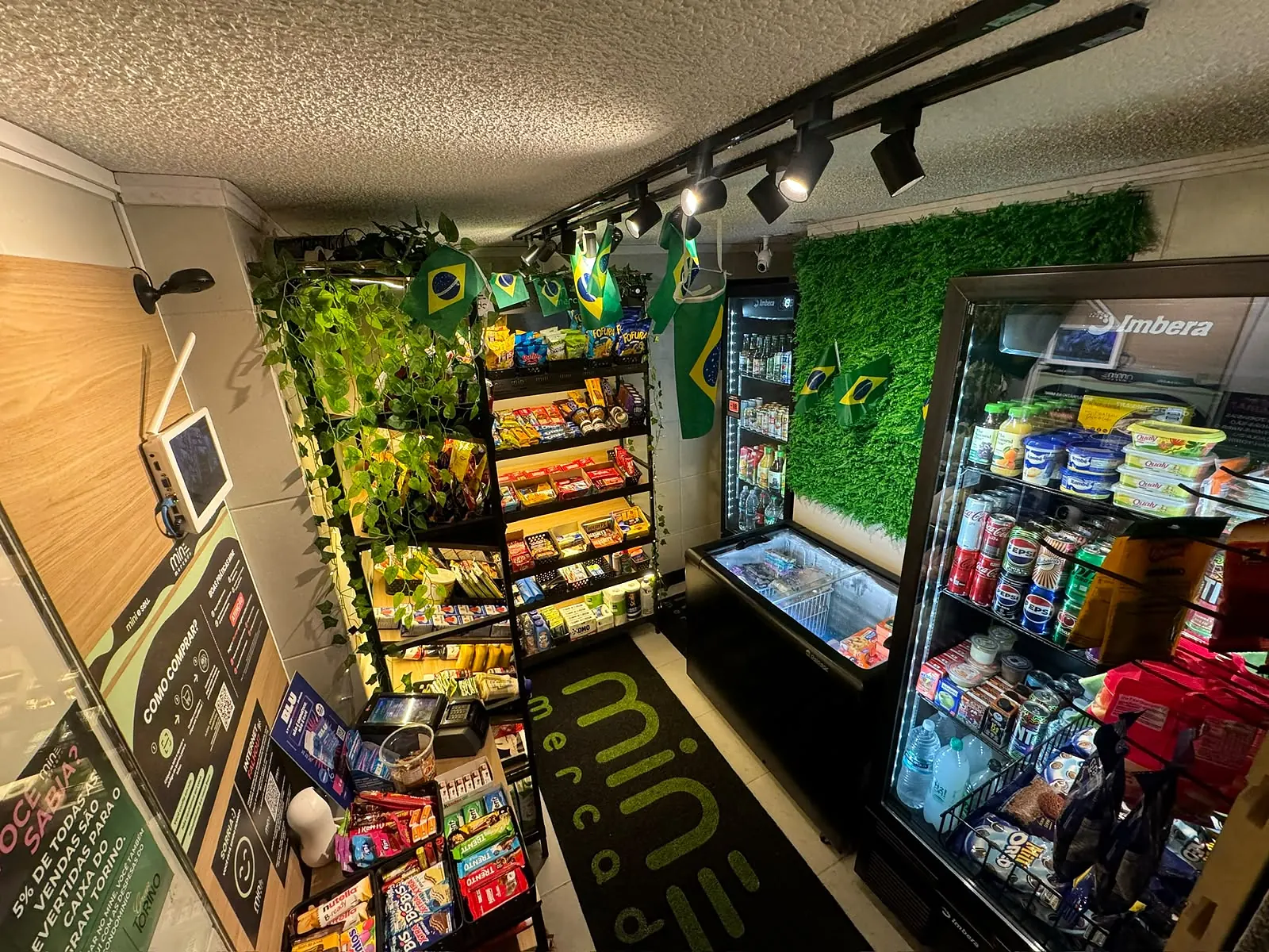 Interior de uma unidade do MINE Mercado com prateleiras, geladeiras, freezer e o tapete da marca no piso